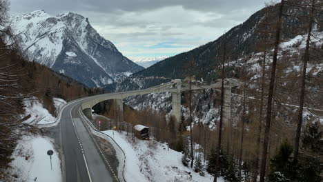 Breite-Drohnenaufnahme-Der-Hochmodernen-Ganterbrücke-Zwischen-Den-Hohen-Schweizer-Gipfeln-Der-Im-Winter-Bedeckten-Alpen