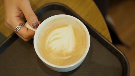 Woman's-Hand-Pick-up-Cup-of-Hot-Latte---top-down-view