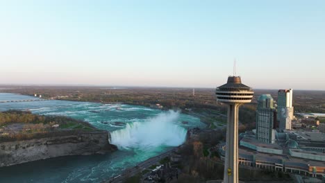 Niagara-falls-from-Canada-side-with-observation-tower-during-sunset,-Drone-descending
