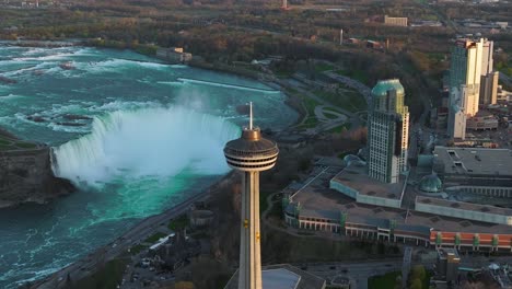 Niagara-falls-from-Canada-side-with-observation-tower-during-sunset,-Drone-orbiting