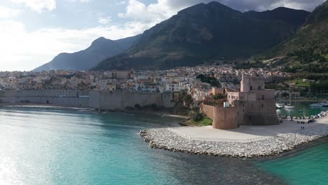 Aerial-Flying-Over-Turquoise-Waters-In-The-Gulf-Of-Castellammare-Towards-Castello-Arabo-Normanno-On-Sunny-Day
