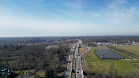 Drone-shot-of-winter-in-Ohio-with-solar-panels-next-to-a-highway-running-through-a-small-town
