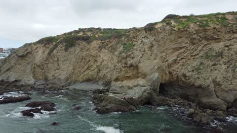 Aerial-Parallax-Of-People-Hiking-Along-The-Rocky-Sea-Caves-Of-Dana-Point,-California