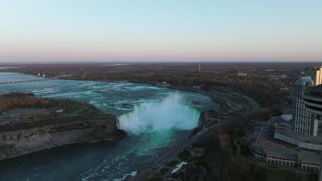 Niagara-falls-from-Canada-side-with-observation-tower-during-sunset,-Drone-flies-backwards