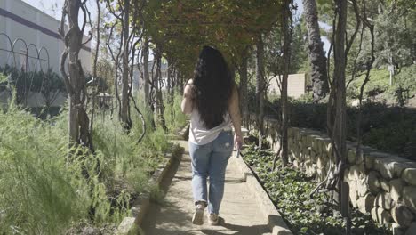 Girl-Walking-Through-Garden-of-Shrubs-and-Vines-while-wearing-jeans