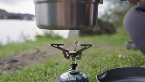 putting-a-pot-on-the-field-cooker-at-the-bank-of-the-loch-during-a-day,-food-preparation