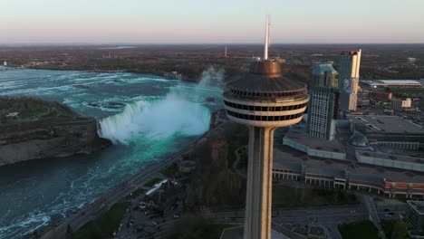 Niagara-falls-from-Canada-side-with-observation-tower-during-sunset,-Drone-flies-sideway