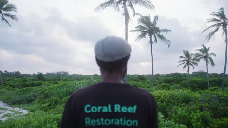Junger-Schwarzer-Mann-In-Einem-T-Shirt-Zur-Wiederherstellung-Des-Korallenriffs,-Der-Den-Exotischen-Grünen-Dschungel-In-Afrika-Betrachtet