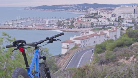 A-parked-mountain-bike-faces-the-stunning-coastal-view-as-cyclists-and-cars-navigate-the-winding,-bendy-road-below
