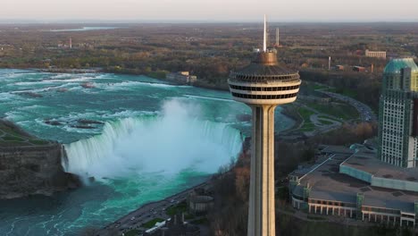 Niagara-falls-from-Canada-side-with-observation-tower-during-sunset,-Drone-rising-and-tilting-down