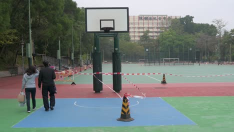 Menschen-Gehen-An-Einem-Leeren-Basketballplatz-Vorbei,-Der-Aufgrund-Des-Ausbruchs-Und-Der-Einschränkungen-Des-Covid-19-coronavirus-In-Hongkong-Auf-Einem-Geschlossenen-Spielplatz-Zu-Sehen-Ist