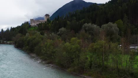 Antenne-Aufsteigend-Durch-Bäume-Am-Fluss-Isel-Mit-Blick-Auf-Schloss-Bruck-In-Österreich
