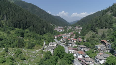 AERIAL:-Flying-above-a-small-village-in-Bulgaria-located-between-two-hills,-surrounded-by-coniferous-forests