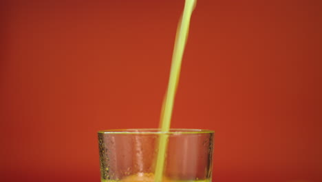 Close-up-slow-motion-footage-of-fresh-orange-juice-pouring-and-spilling-in-a-highball-glass,-isolated-on-an-orange-background
