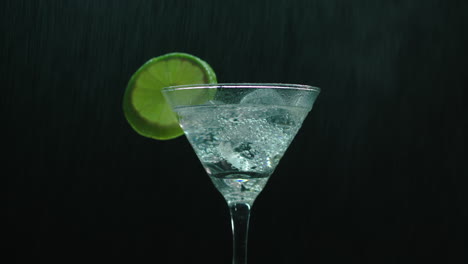 Rotierendes-Martini-Glas,-Das-Mit-Einer-Wasserkanne-Besprüht-Wird-Und-Einen-Kühlen-Regeneffekt-Erzeugt