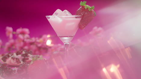 Video-product-composition-of-a-martini-glass-with-a-strawberry-milkshake,-surrounded-by-fresh-strawberries,-pomegranates-and-candles