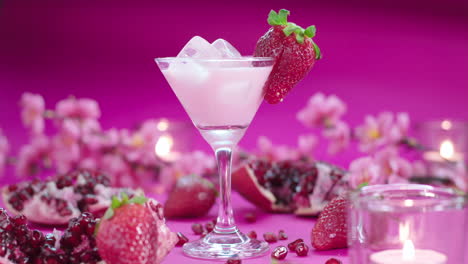 Colorful,-vibrant-video-product-composition-of-a-martini-glass-with-a-strawberry-milkshake,-surrounded-by-fresh-strawberries,-pomegranates-and-candles