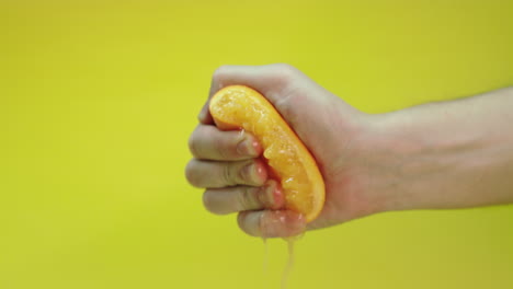 Man-squeezing-an-orange-to-make-fresh-orange-juice-cocktail,-isolated-on-a-yellow-background,-slow-motion-footage