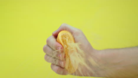 Fresh-orange-squeezed-by-a-man,-causing-the-juice-to-fly-to-the-camera-lens,-slow-motion-footage