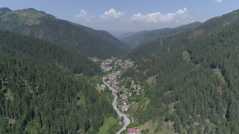 Luftbild:-Flug-über-Einem-Kleinen-Dorf-In-Bulgarien,-Das-Zwischen-Zwei-Hügeln-Liegt-Und-Von-Nadelwäldern-Umgeben-Ist