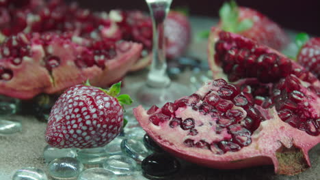 Rotierendes-Produktvideo-Von-Frischen-Erdbeeren-Und-Granatäpfeln-Mit-Strandsand-Und-Glänzenden-Tönen-Als-Dekoration