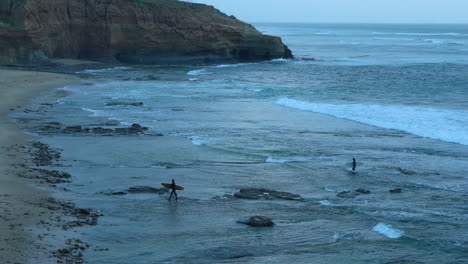 Two-surfers-leaving-the-water-at-dusk-at-Sunset-Cliffs,-San-Diego-California