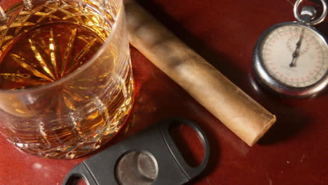 Whiskey-glass,-cigar,-cigar-cutter-and-old-pocket-watch-sit-on-mahogany-bar-top