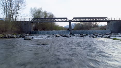 Nahaufnahme-Und-Schnelle-Drohnenaufnahme-über-Einem-Fluss-Vor-Einer-Brücke,-4k-Uhd