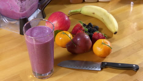 Beauty-shot,-full-glass-of-fruit-smoothie-and-fruit-on-wood-butcher-block-counter