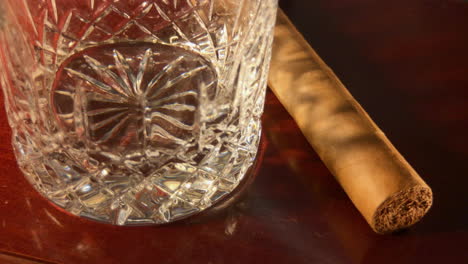Close-up-of-empty-crystal-glass-and-cigar-coming-out-of-shadow