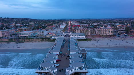 Drone-flying-backwards-over-Crystal-Pier-in-Pacific-Beach,-a-coastal-community-in-San-Diego,-California