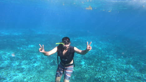 A-boy-freestyle-diving-in-deep-blue-sea-and-cheering-with-peace-sign-enjoying-diving-experience-|-Tourist-diving-in-ocean-with-gears,-mask,-life-jacket-and-fins-on