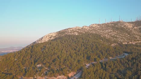 Forward-aerial-shot-of-mountain-Ymittos-in-Athens,-showing-an-array-of-antennas-during-golden-hour
