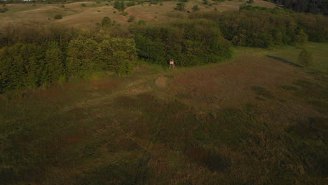 Aerial-View-Of-A-Hunting-Hut-At-A-Meadow,-Morning,-Lens-Flare