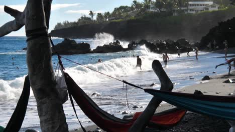 A-wave-crashes-on-people-having-fun-during-Hawaiian-summer-on-Kahena-Blacksand-beach-in-Hawaii-Big-Island