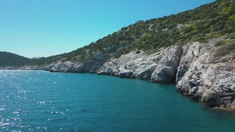 Forward-drone-shot-next-to-a-rocky-shore-in-the-aegean-sea,-Greece