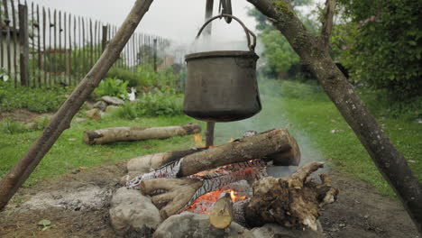 Witch-kettle-steaming-over-fire,-tripod-holding-big-pot-over-burning-flames,-wide-shot