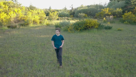 Handsome-teenage-boy-walking-through-beautiful-green-surroundings,-with-his-hands-in-his-pockets