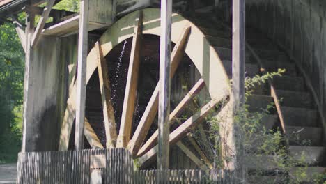 Slow-motion-close-up-of-a-gigantic-historic-ancient-wooden-water-wheel-of-a-watermill-spinning-while-water-is-flowing-on-it,-splashing-it-around