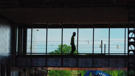 Silhouetted,-slow-motion-shot-of-a-construction-worker-crossing-a-bridge-walkway