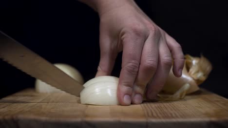 Close-up-shot-of-lady-cutting-onions-on-cutting-board-with-black-background