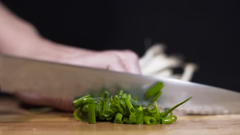 Close-up-shot-of-lady-cutting-spring-onions-scallions-on-cutting-board-with-black-background