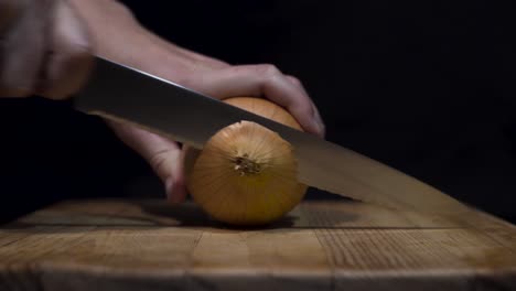 Close-up-shot-of-lady-cutting-onions-on-cutting-board-with-black-background