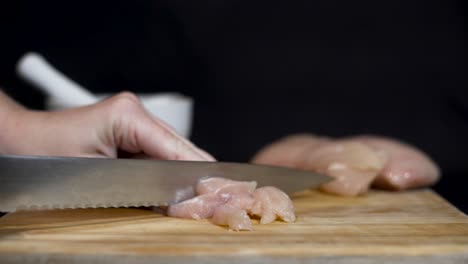 Close-up-shot-of-lady-cutting-raw-chicken-fillets-and-adding-salt-on-cutting-board-with-black-background
