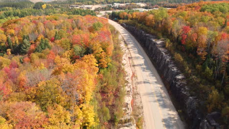 Aerial-view-around-a-road-in-middle-of-autumn-foliage-in-sunny-Canada---circling,-drone-shot