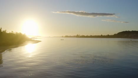 Two-kayaks-sailing-along-the-Australian-coast-into-the-sunset,-trees,-blue-sky