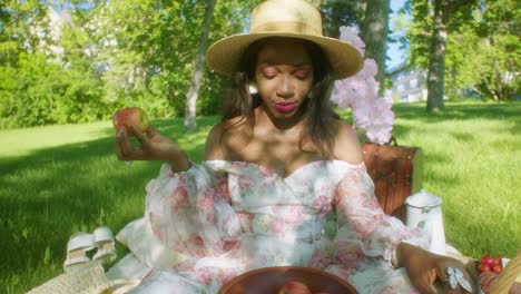 Mujer-Negra-Comiendo-Manzana-Y-Ajustando-El-Cabello-En-Un-Picnic-En-El-Parque