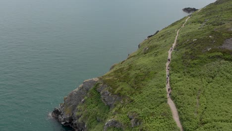 Drone-flying-and-people-walking-on-a-small-path-in-a-large-mountain-near-the-sea-on-a-sunny-day