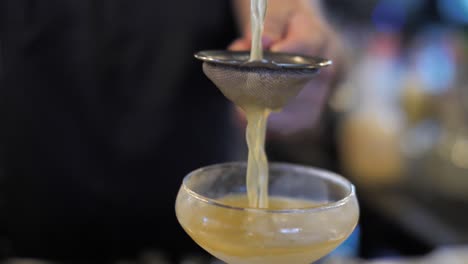 Professional-bartender-poring-fruit-cocktail-into-glass-though-sieve,-close-up