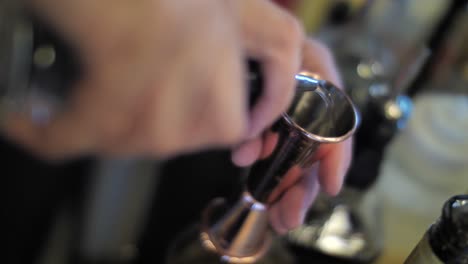 Pouring-liquor-into-metal-measure-glass-to-prepare-alcohol-cocktail,-close-up
